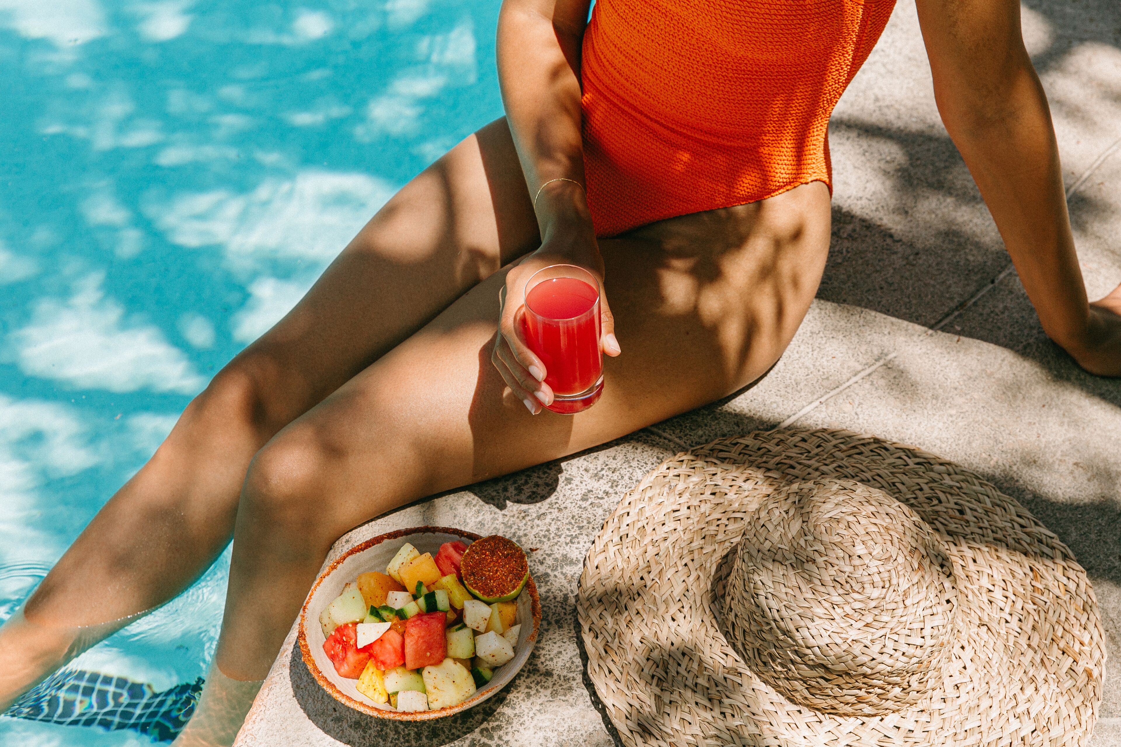 A person sitting by a pool with a drink and a fruit bowl.