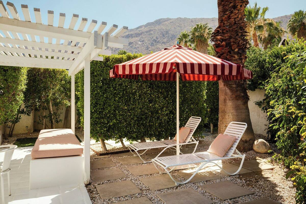 Un patio con dos sillones de descanso, una sombrilla a rayas y una pérgola.