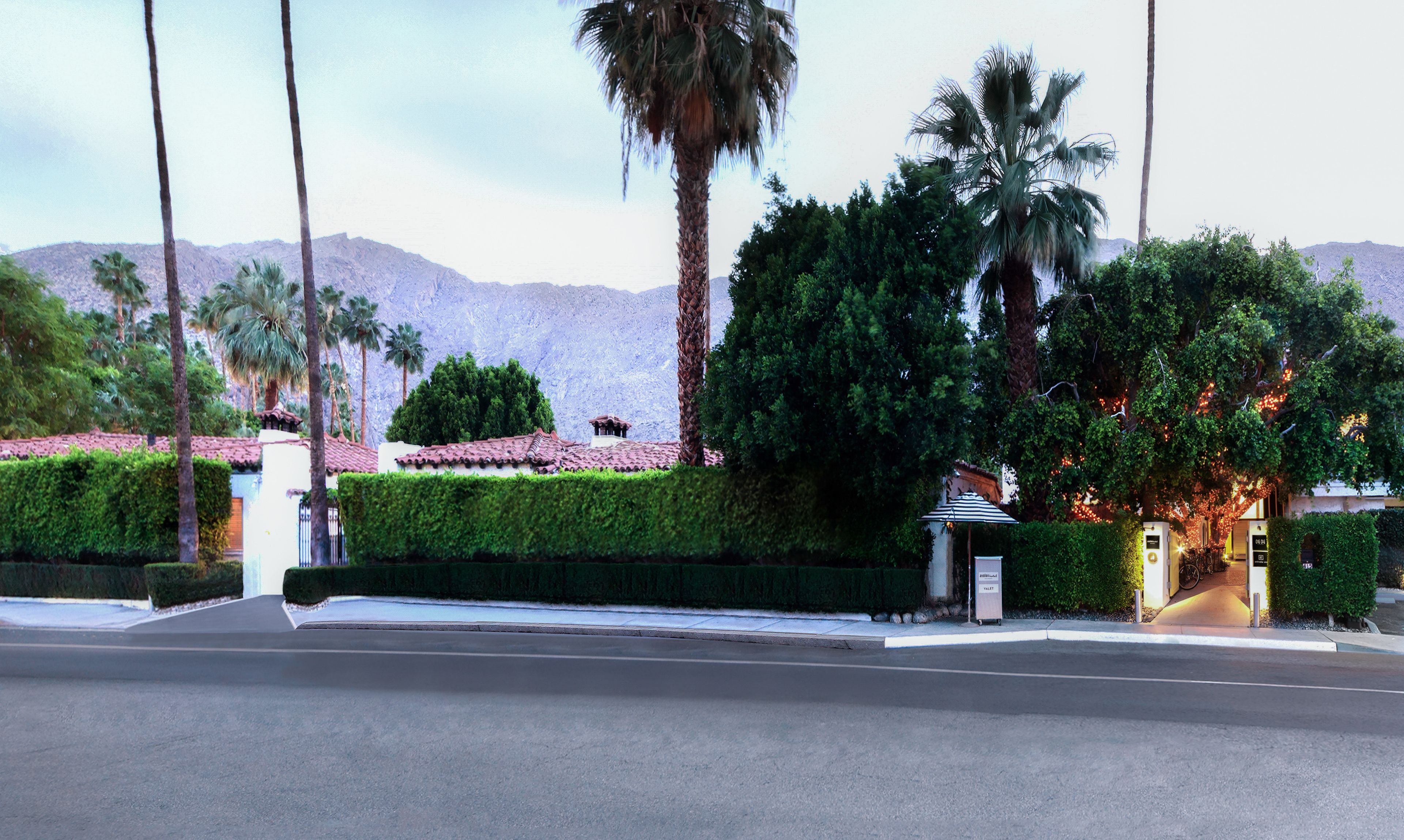 A hotel with a well-maintained garden, a parking area, and a mountain backdrop.