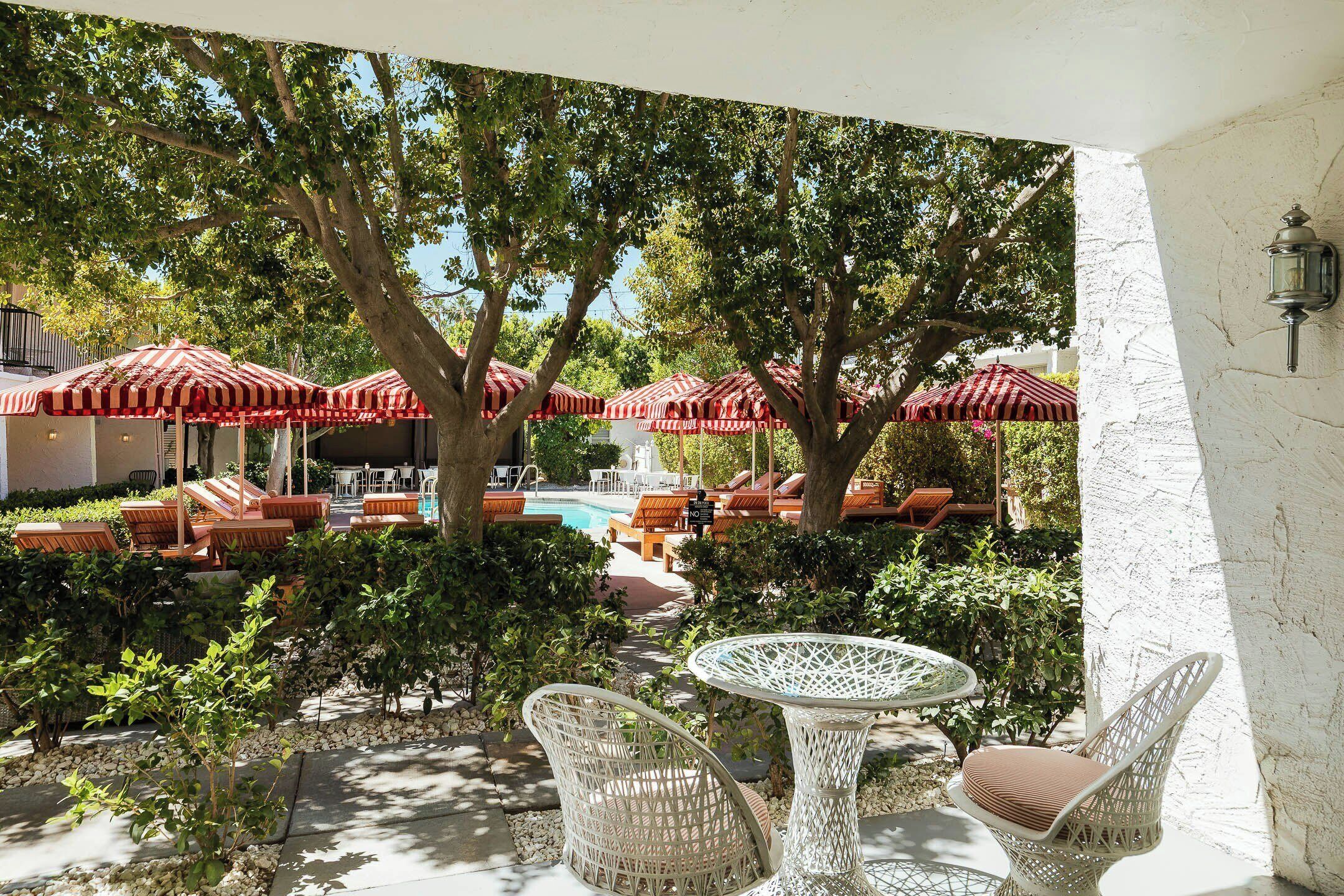 A patio area with wicker furniture, red-striped umbrellas, and a pool in the background.