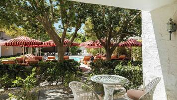 A patio area with wicker furniture, red-striped umbrellas, and a pool in the background.