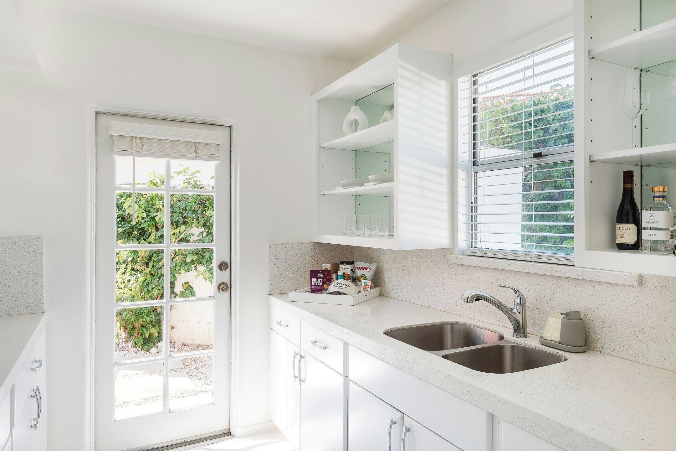 A kitchen with a double sink, white cabinets, and a window with blinds.