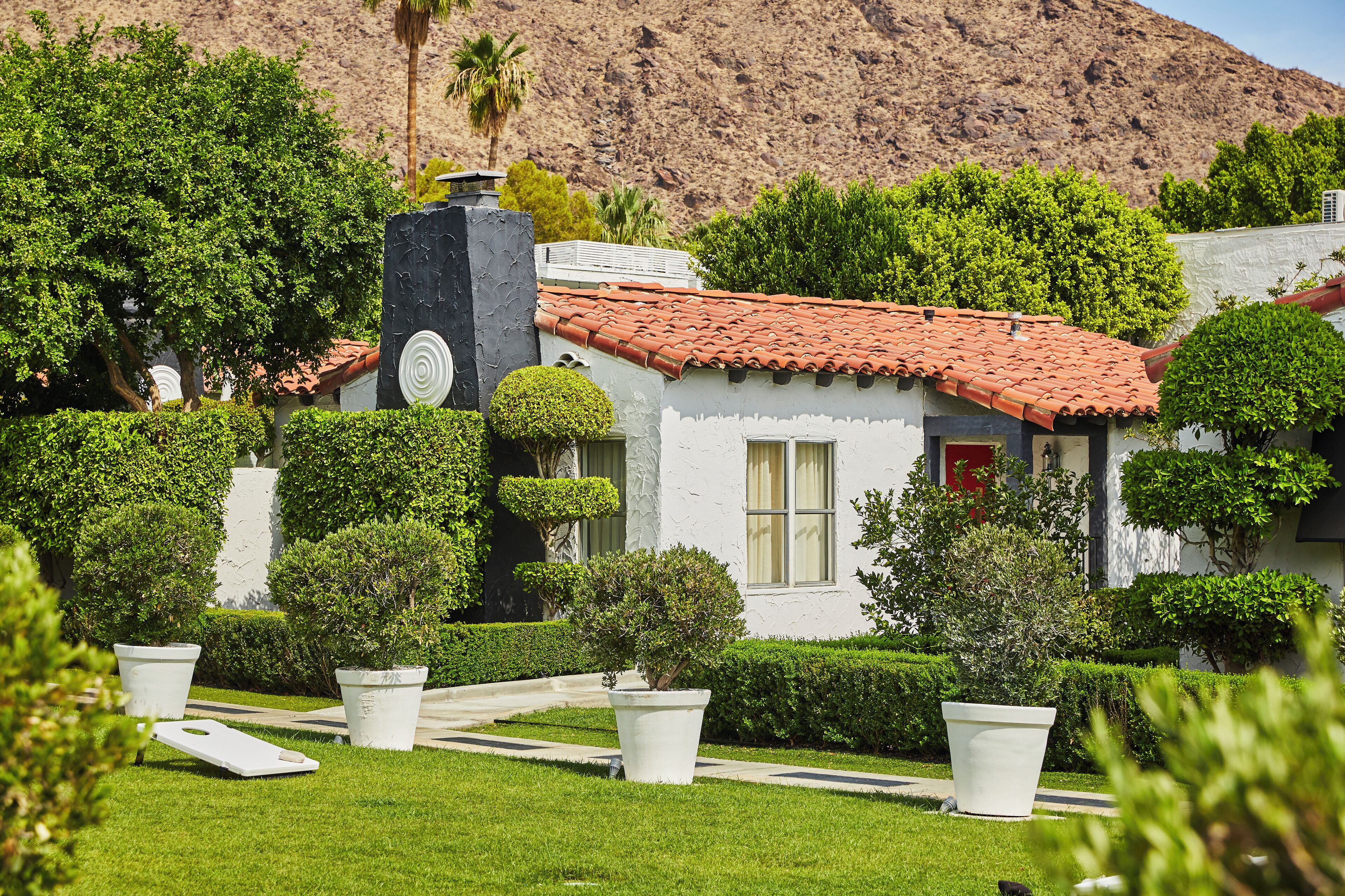 A white building with a red-tiled roof, surrounded by well-maintained hedges and potted plants.