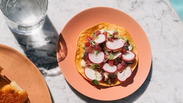 A plate with a tortilla topped with radishes and greens, a glass of water, and a slice of bread on a marble table.