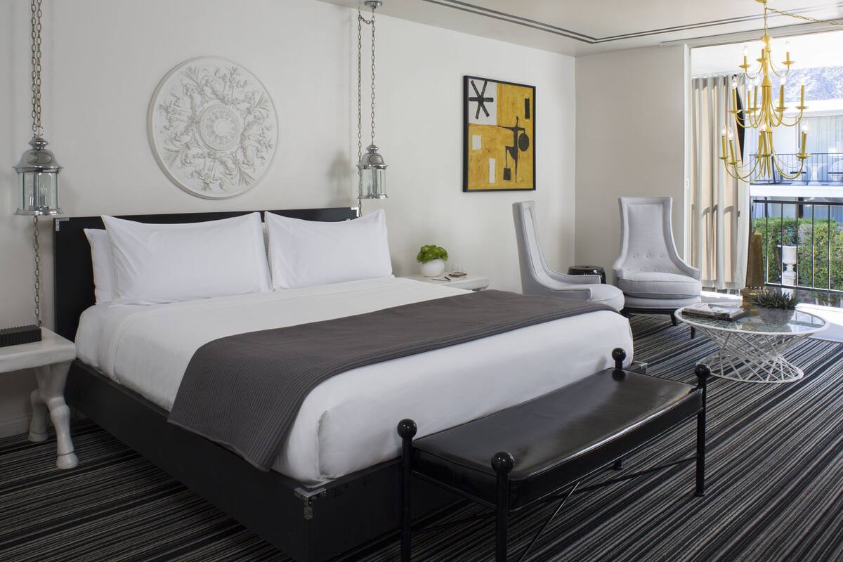 Une chambre d’hôtel moderne avec un grand lit, un lustre, une table de chevet, une chaise et une vue sur l’extérieur.