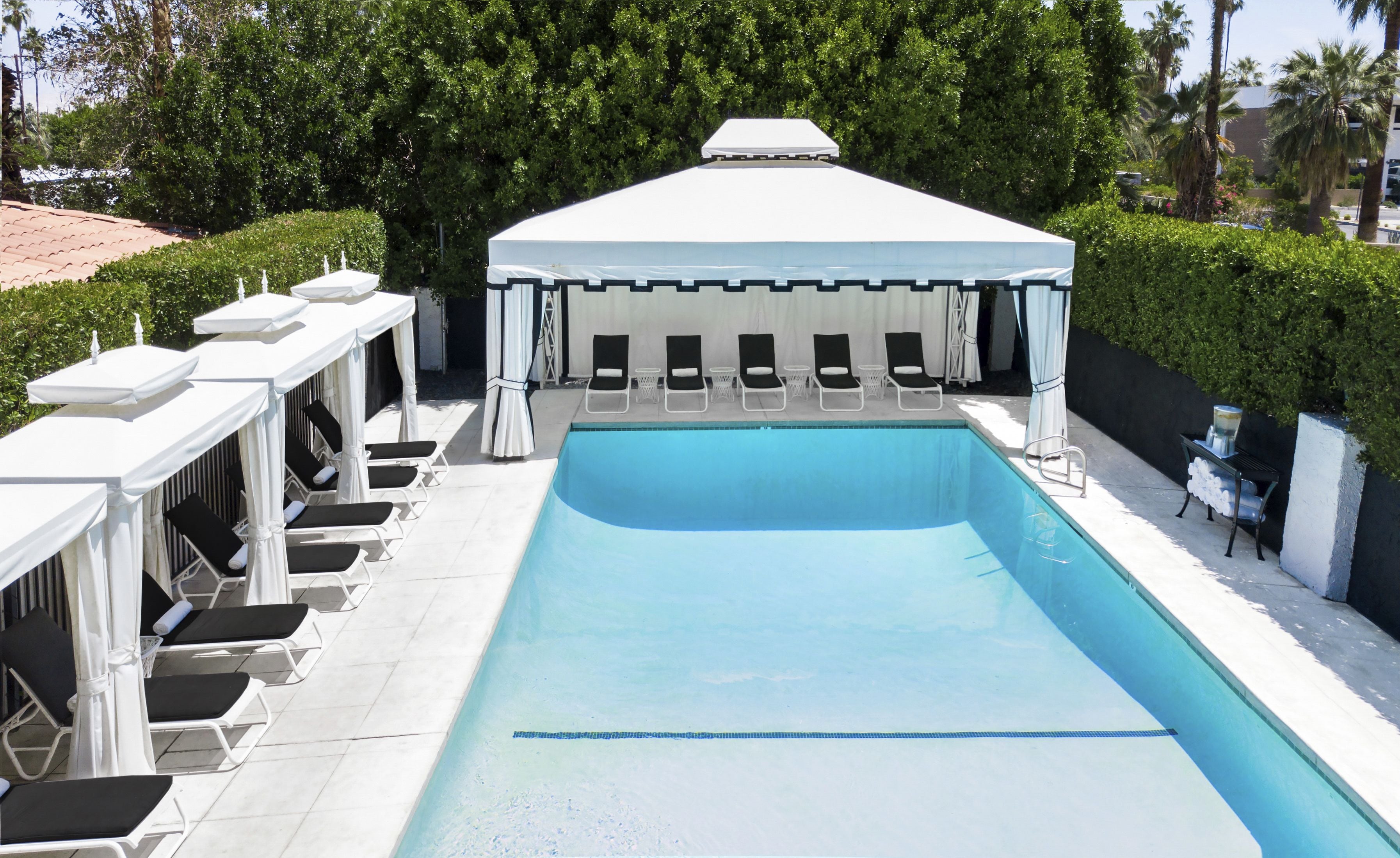 Une piscine rectangulaire dotée d’un auvent blanc et de chaises longues.