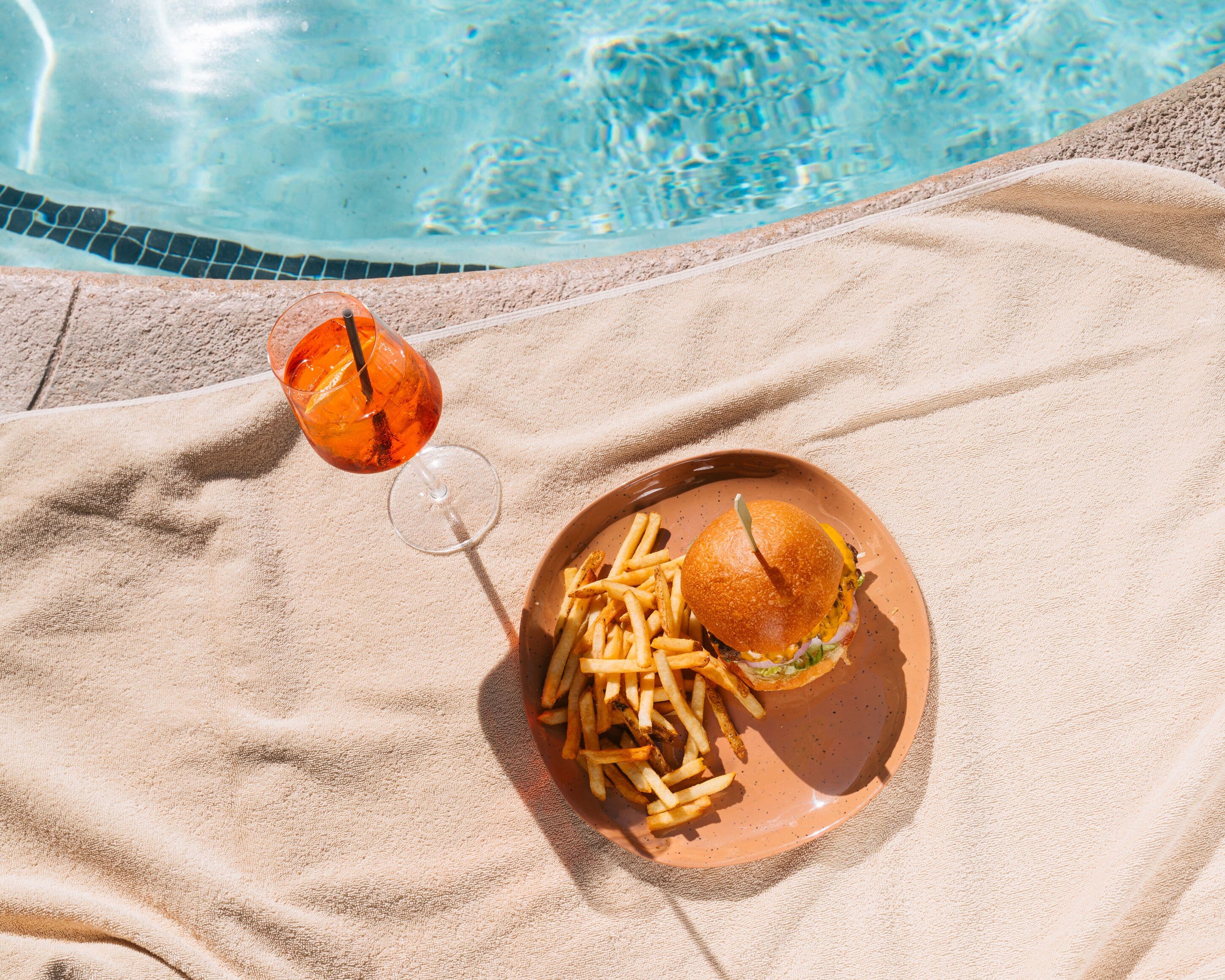 A dining setup by a poolside with a plate of food and a drink.