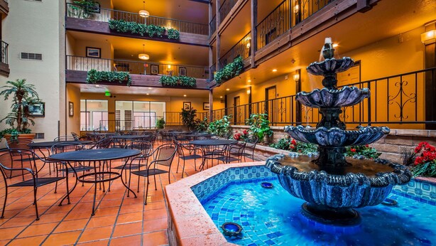 A hotel atrium with a fountain, outdoor seating, and multiple balconies with plants. - Best Western El Grande Inn (Clearlake)