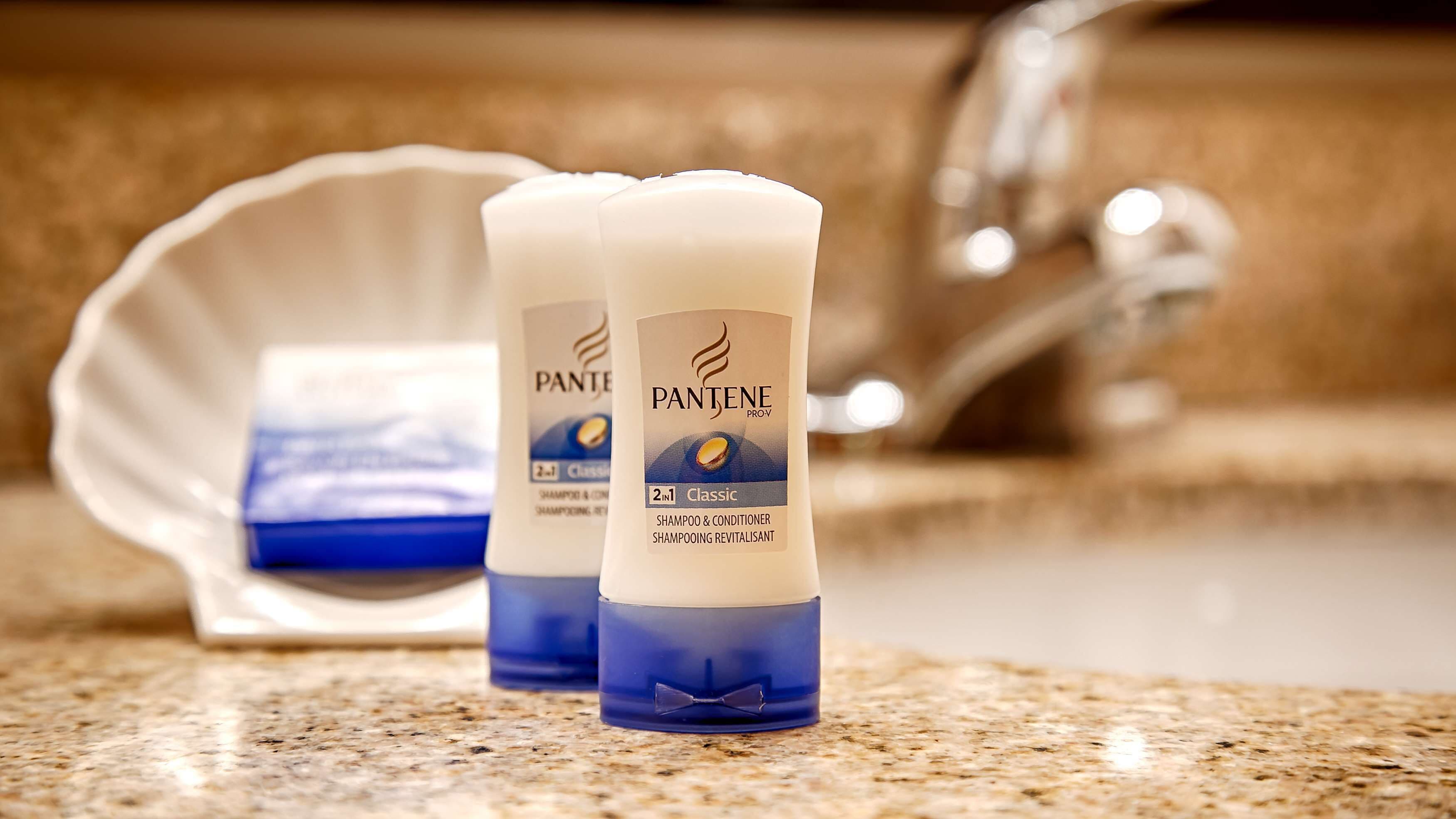 Deux bouteilles de shampoing et d’après-shampoing Pantene Pro-V Classic sont posées sur un comptoir en granit, avec un évier et un porte-savon en arrière-plan.