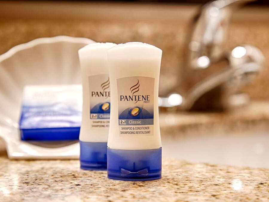 Deux bouteilles de shampoing et d’après-shampoing Pantene Pro-V Classic sont posées sur un comptoir en granit, avec un évier et un porte-savon en arrière-plan.
