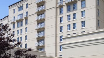A multi-story hotel with a flat facade, balconies on each floor, and a landscaped garden area in front.