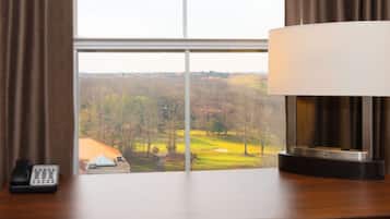 A hotel room with a desk, a lamp, a telephone, and a view of a golf course through a window.