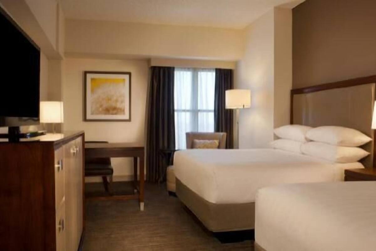 A hotel room with two beds, a desk, a chair, a television, and a window with curtains.