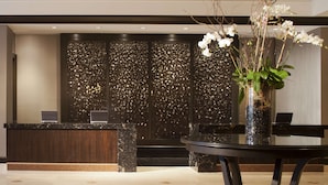 A reception area with a dark wood reception desk, two laptops, a vase with white flowers, and a glass table. - Hyatt Regency Long Island (Hauppauge)