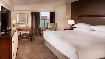 A hotel room with a large bed, a desk with a chair, a television, and a window with curtains.