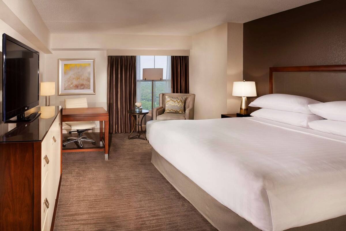 A hotel room with a bed, a desk, a chair, a TV, and a window with curtains.