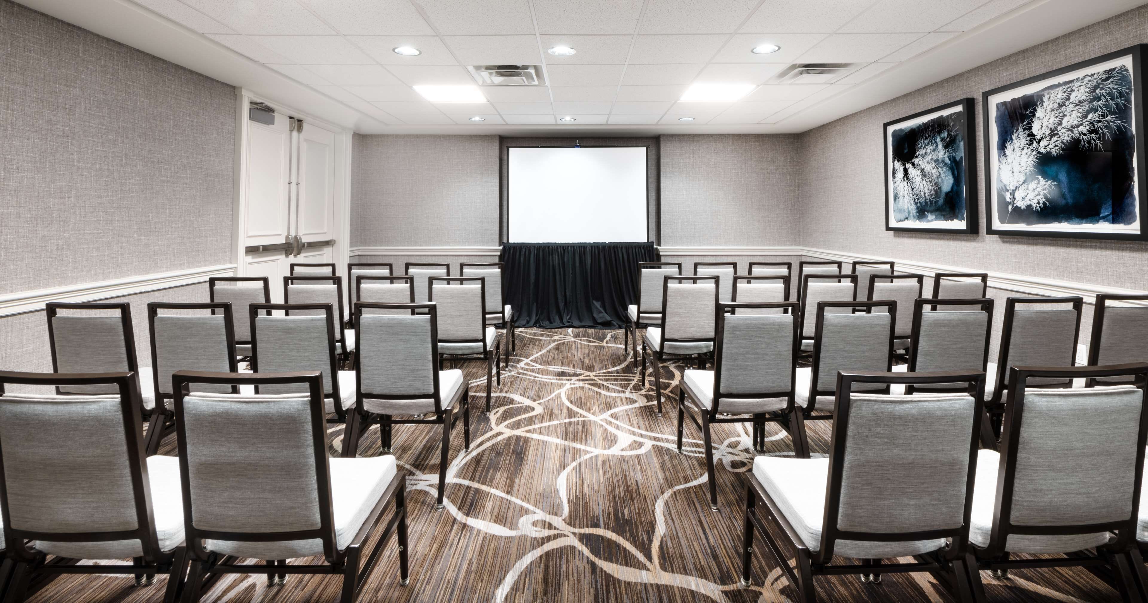A conference room with rows of chairs, a projector screen, and two framed artworks on the walls.