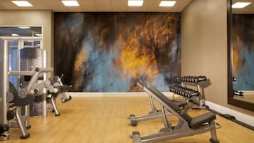 Une salle de sport équipée de matériel d’exercice, dotée d’un plancher en bois et ornée d’une grande fresque murale abstraite.