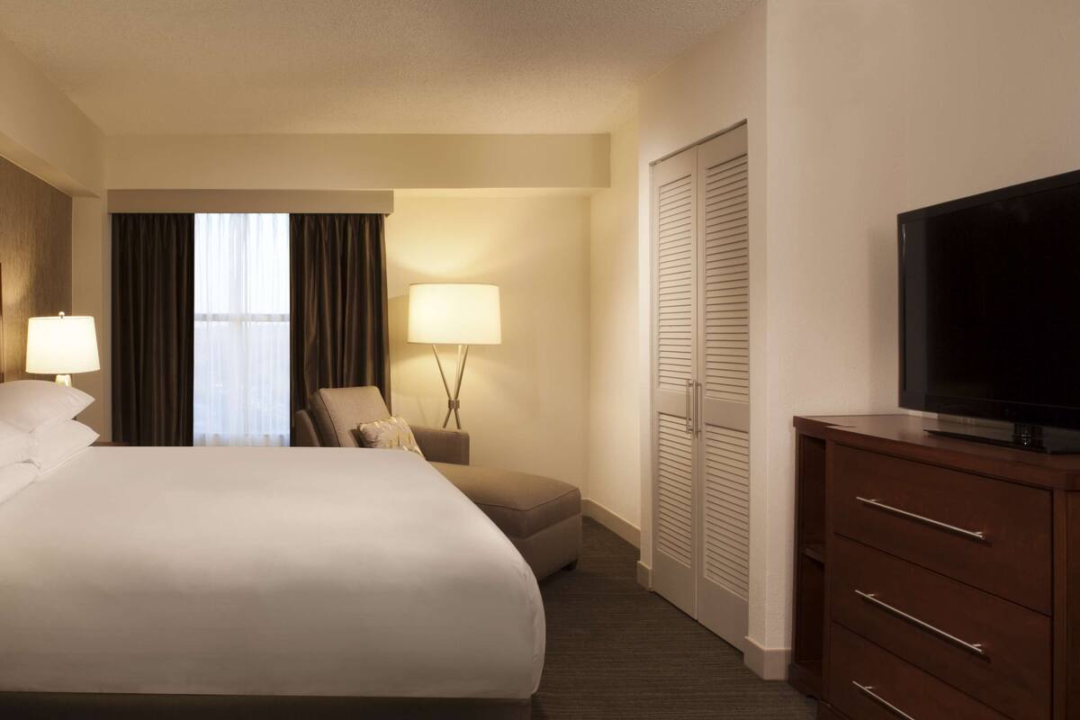 A hotel room with a large bed, two bedside lamps, a TV, a chair, a desk, and a wardrobe.