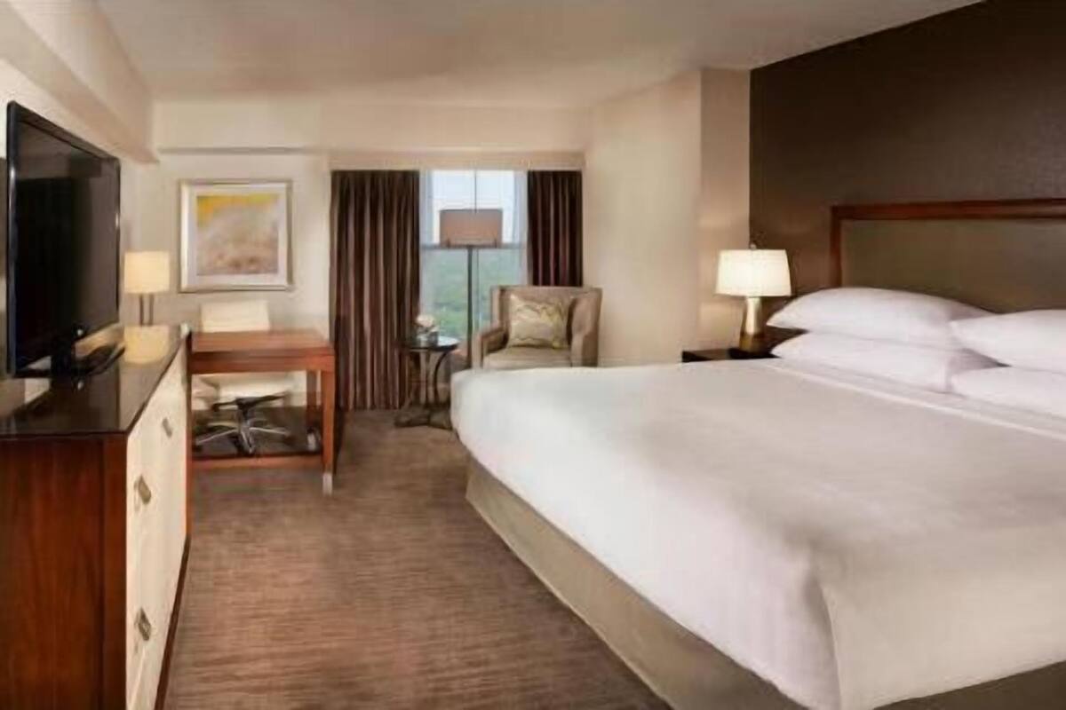 A hotel room with a bed, a desk, a chair, a TV, and a window with curtains.