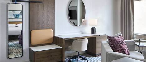 A hotel room with a desk, a chair, a sofa, a mirror, and a window with curtains.