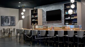 Un bar moderno con una barra alargada, varios taburetes y estantes llenos de botellas.