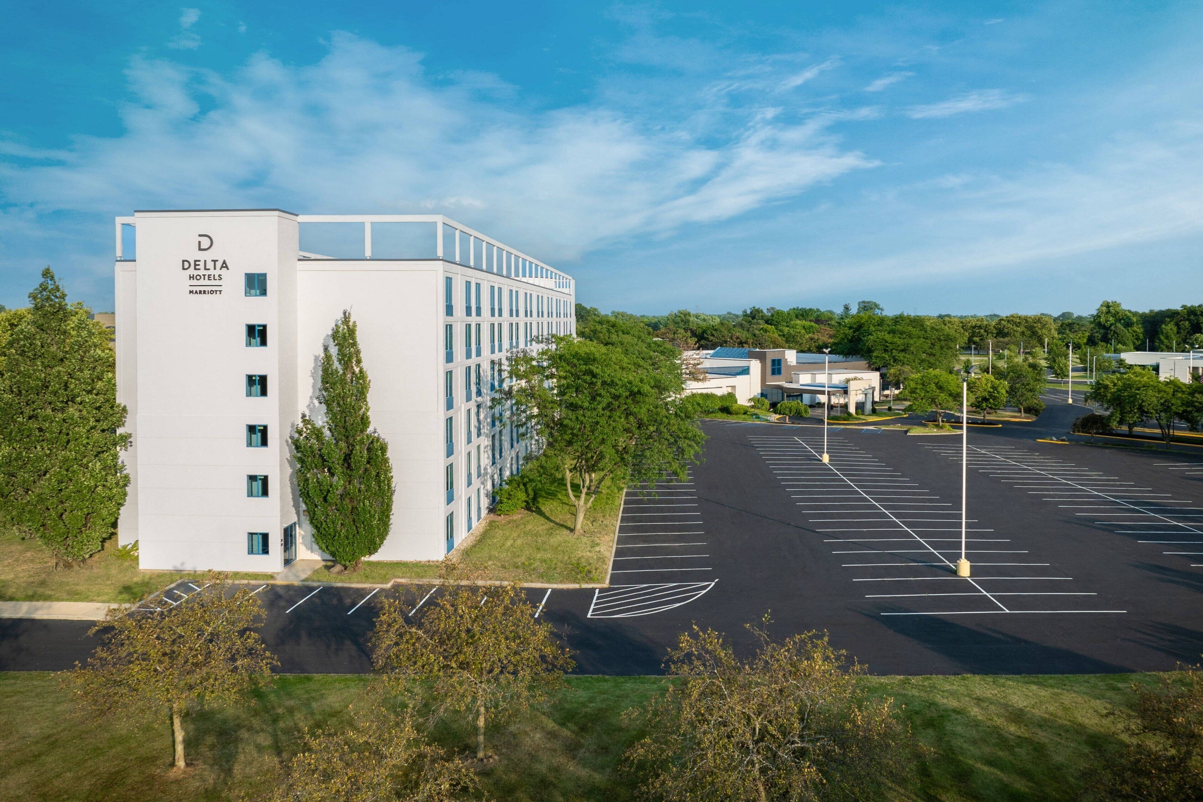 A modern Delta Hotels Marriott building with a parking lot and surrounding greenery.