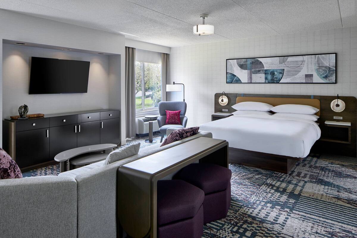 Ein modernes Hotelzimmer mit einem großen Bett, einem Flachbildfernseher, einem Schreibtisch und einer gemütlichen Sitzecke.