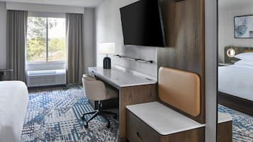 Une chambre d’hôtel équipée d’un lit, d’un bureau, d’une chaise, d’une télévision et d’une fenêtre avec des rideaux.