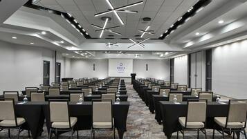A conference room with rows of tables and chairs, a carpeted floor, and a modern ceiling design.