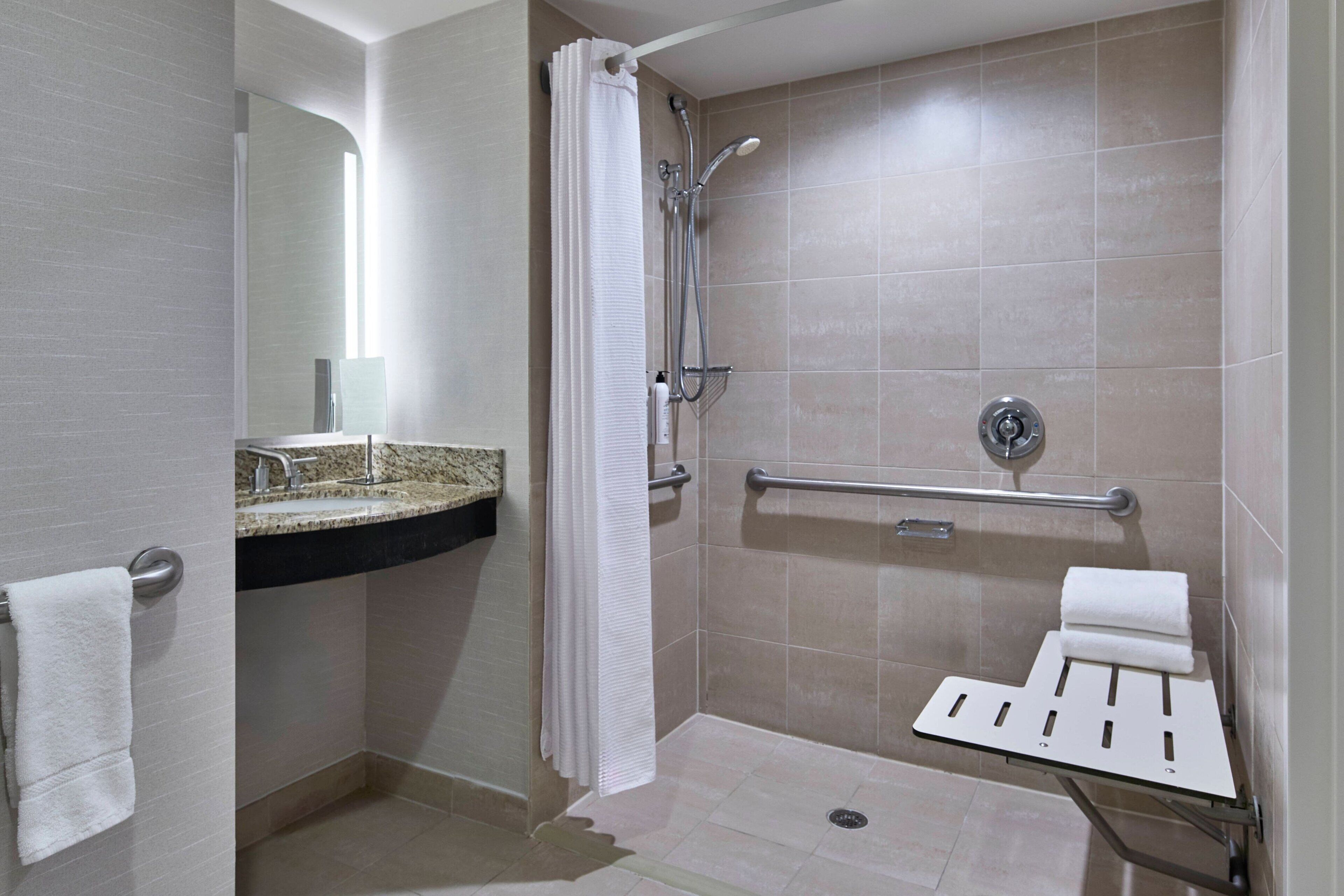Un baño moderno con ducha, un lavamanos con encimera de granito, una barra de apoyo y un perchero.