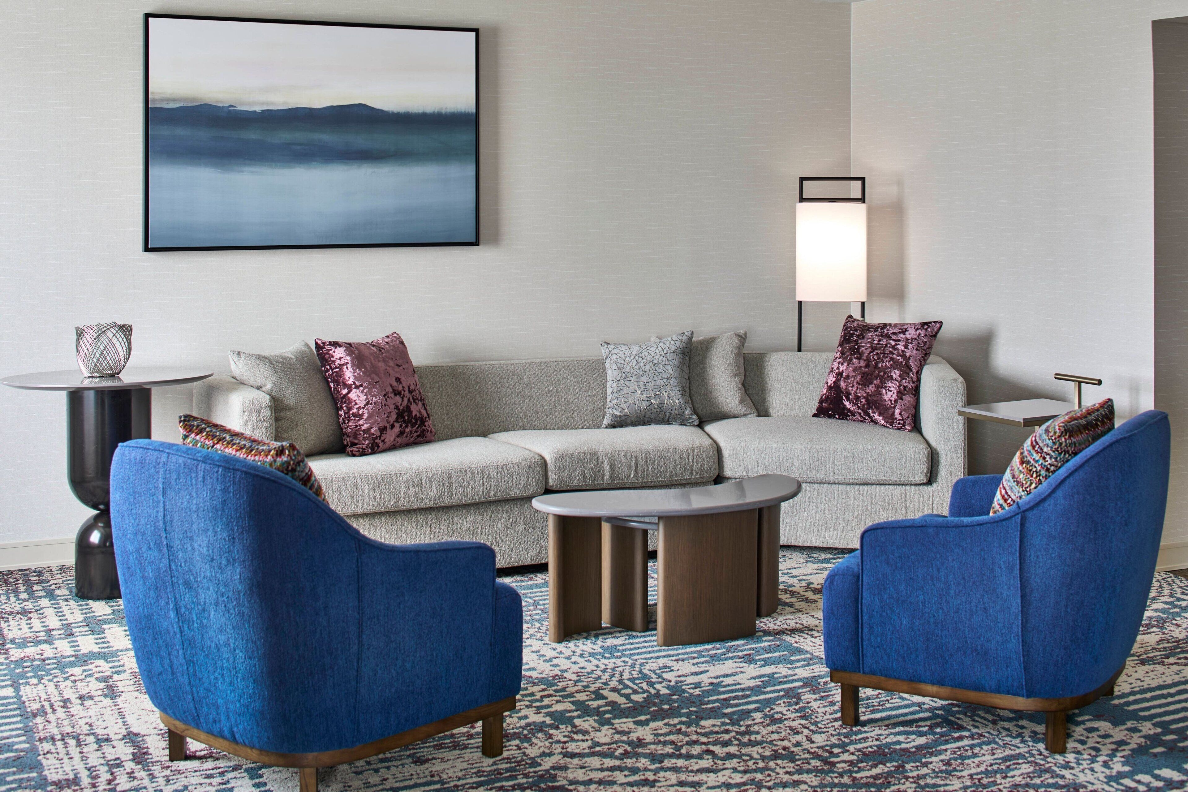 A modern living room with a grey sectional sofa, two blue armchairs, a round coffee table, and a floor lamp.