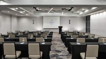 A conference room with rows of tables and chairs, a podium, and a screen displaying the Delta Hotels Marriott logo.