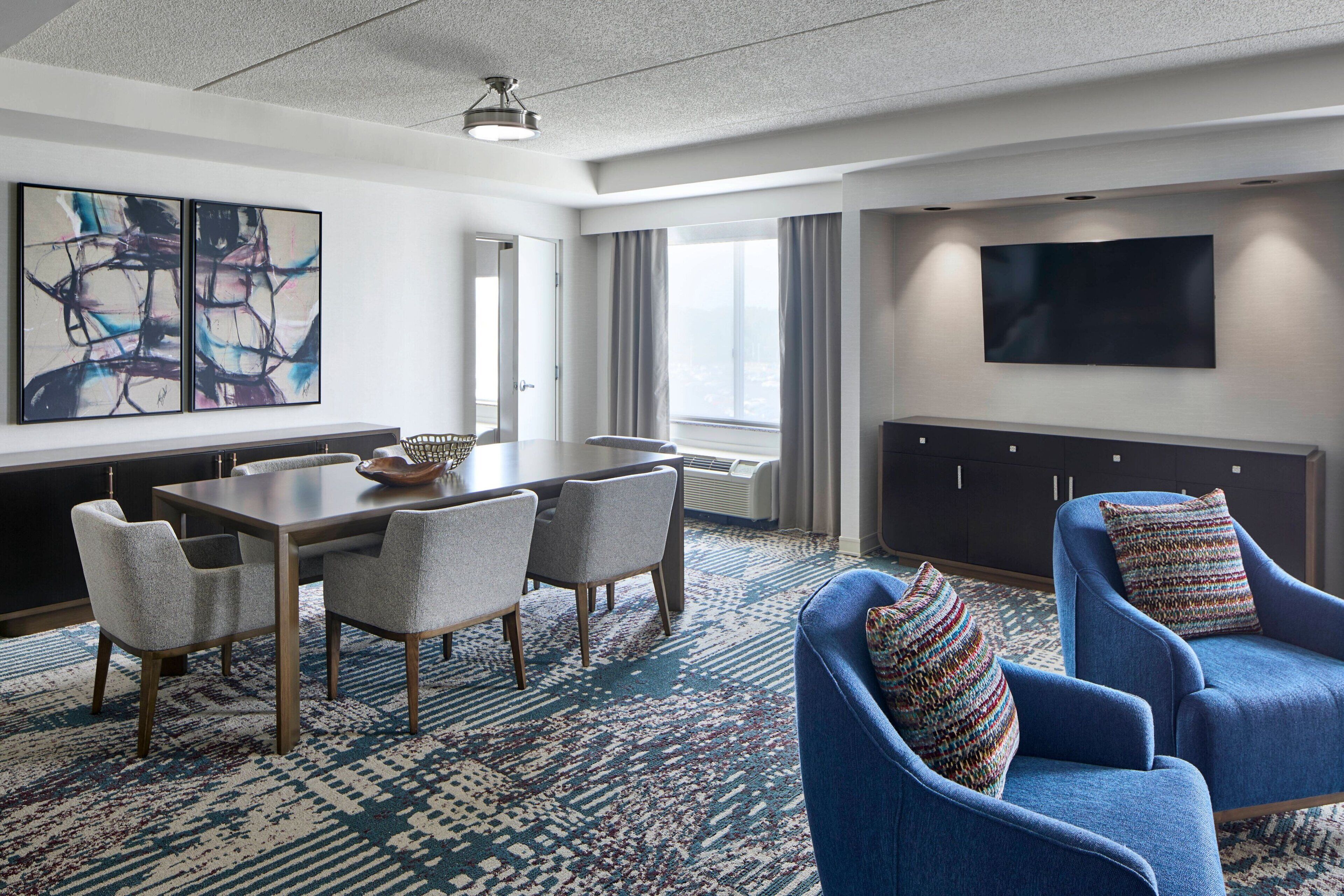 Ein modernes Hotelzimmer mit Essbereich, großem Flachbildfernseher und Blick auf die Stadt.
