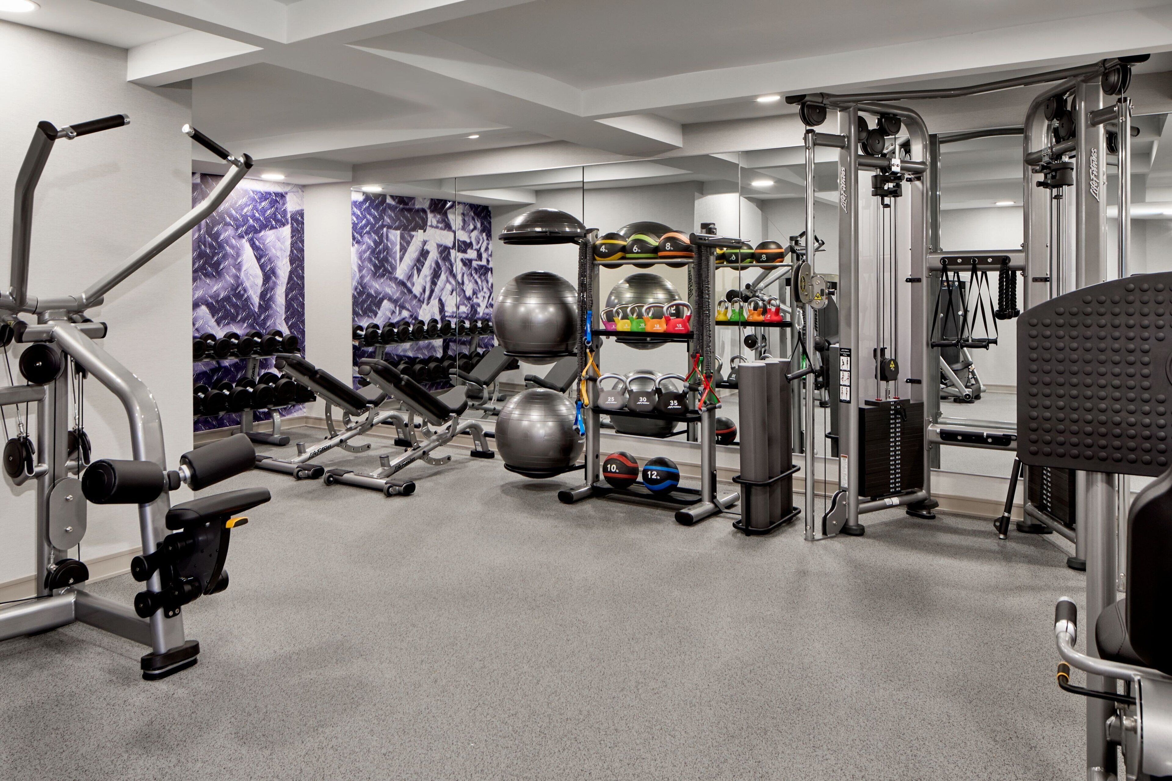 Un gimnasio con diversos equipos de ejercicio, estantes para pesas y un espejo grande.
