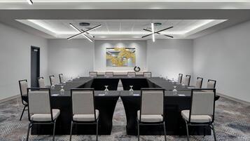 Un salón de conferencias con una larga mesa, sillas y un elemento decorativo en la pared.