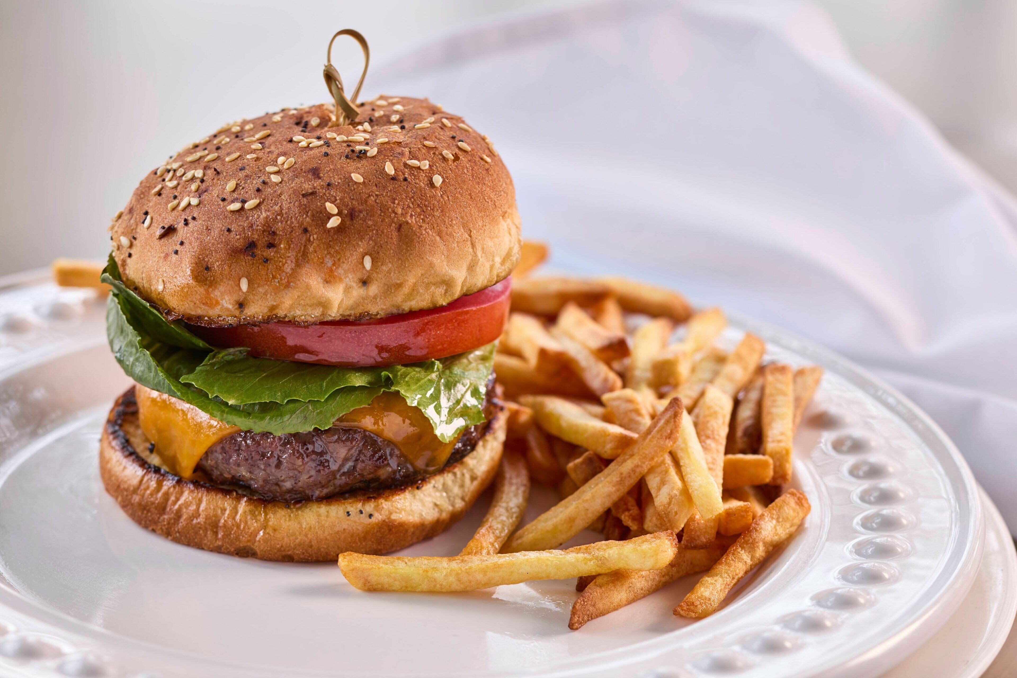 A hamburger with lettuce, tomato, and cheese, and a side of French fries on a white plate.