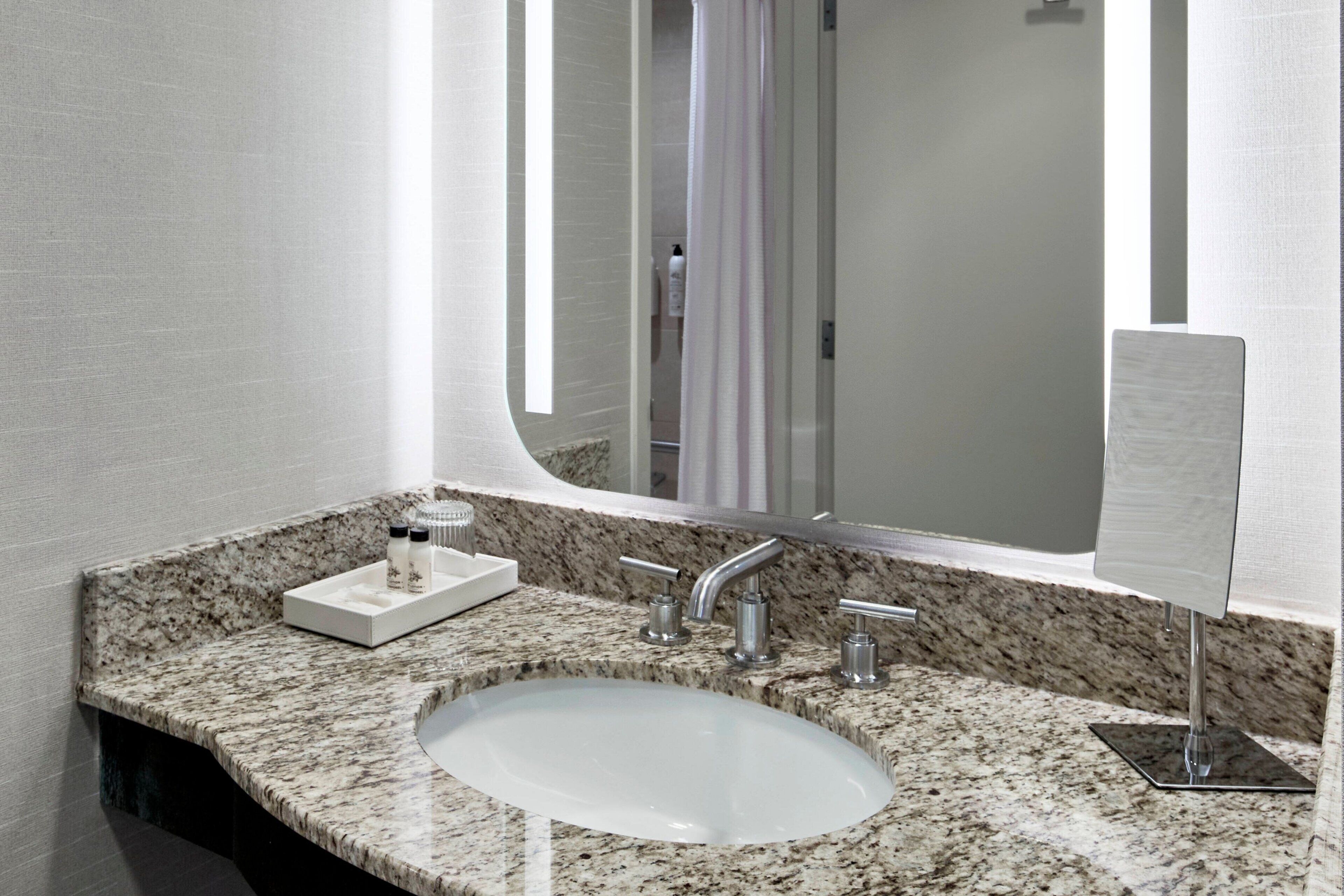 A bathroom with a granite countertop, a white sink, and a large mirror.
