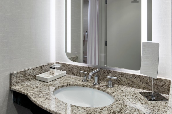 Un baño con encimera de granito, un lavamanos blanco y un espejo grande.