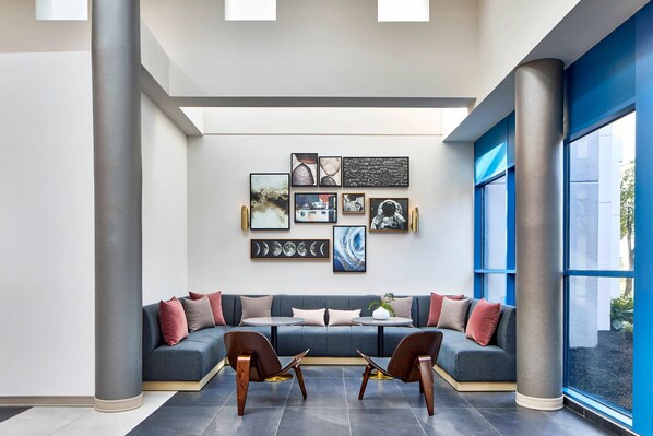 Un intérieur moderne avec un canapé gris, deux chaises en bois et un mur orné d’œuvres d’art encadrées.