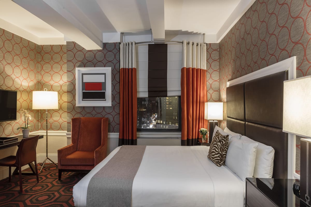 A hotel room with a large bed, a desk, a chair, a TV, and a window with curtains.