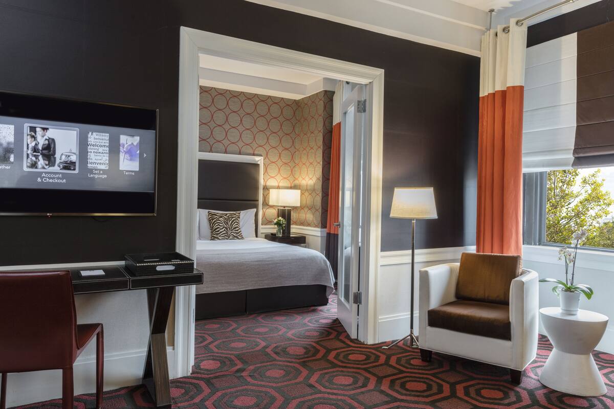 A hotel room with a bed, desk, chair, TV, and a view of the outdoors.