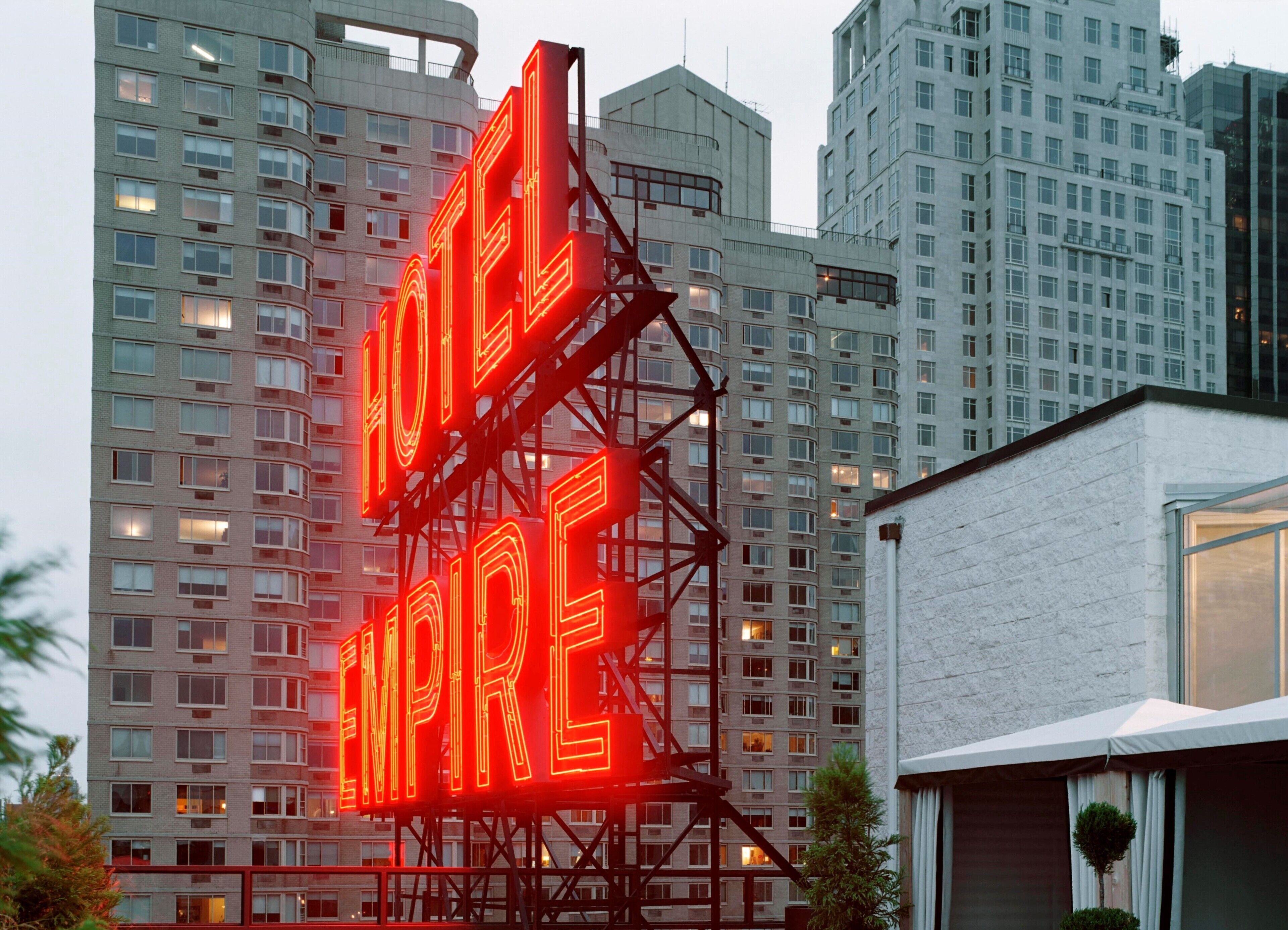 Un hôtel reconnaissable à son grand panneau néon rouge sur lequel on peut lire « HÔTEL EMPIRE », entouré d’immeubles de grande hauteur.