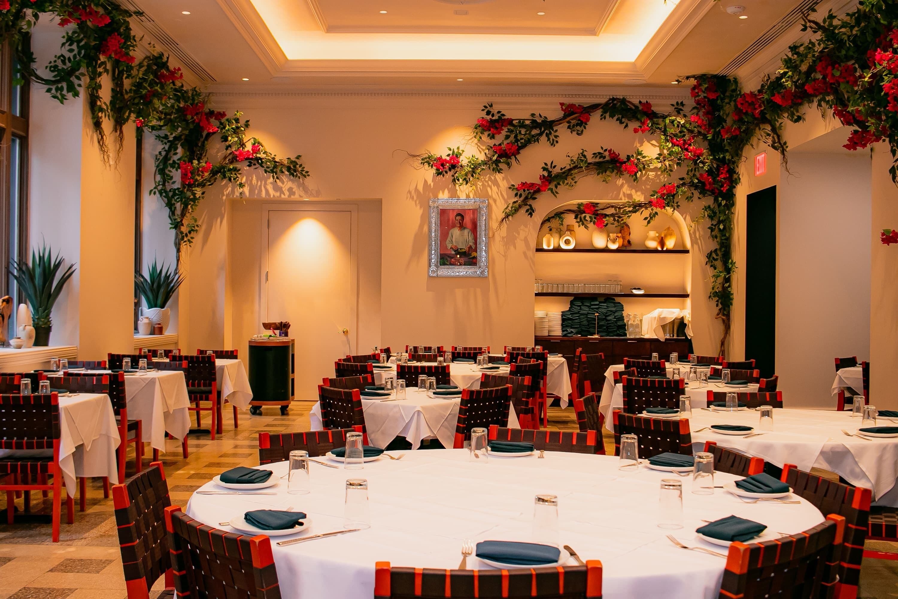 Un comedor con mesas redondas, sillas rojas y negras, y decoraciones florales.