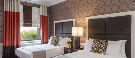 Een hotelkamer met twee bedden, een groot raam met gordijnen, een hoofdeinde met een lamp en een kamer met een patroon op de muur.