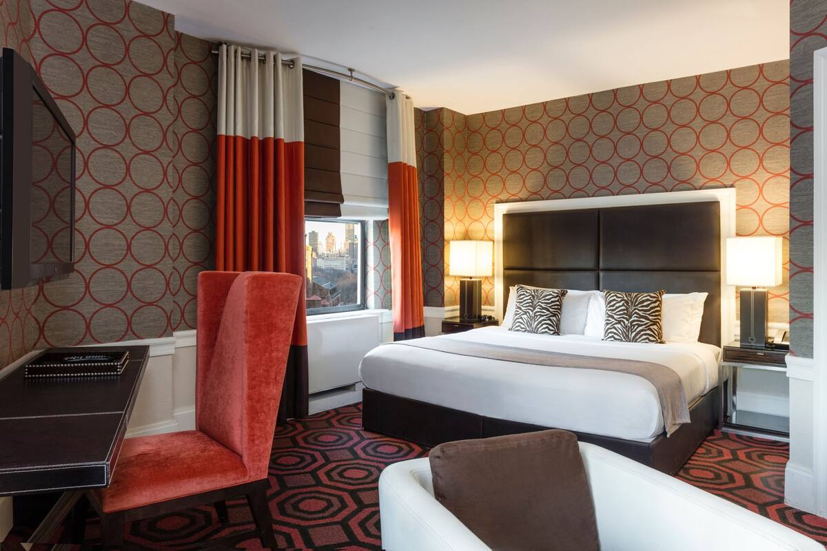 A hotel room with a large bed, a desk, and a chair.