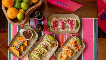 Una mesa con diferentes platillos, entre ellos tacos y un tazón de frutas.
