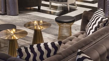 Un salón moderno con un sofá gris oscuro, mesas redondas doradas y cojines estampados.