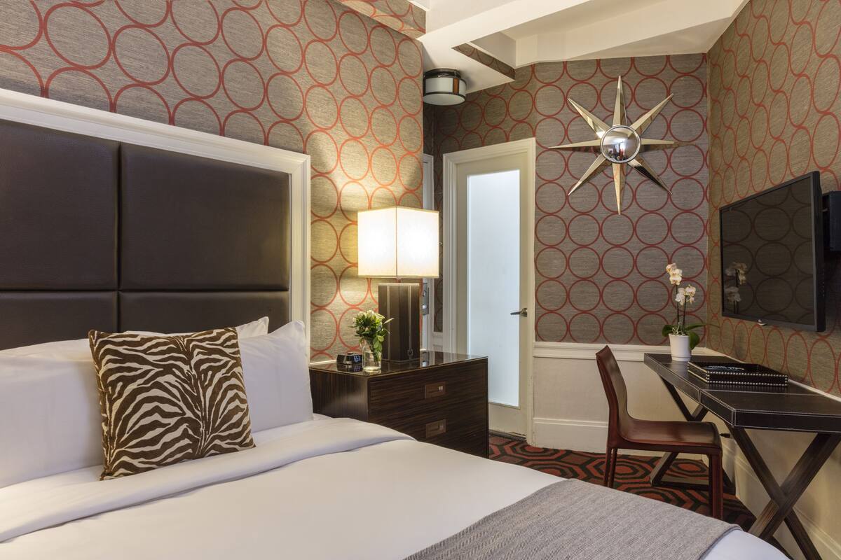 A hotel room with a large bed, a desk, a chair, a TV, and a decorative wall clock.