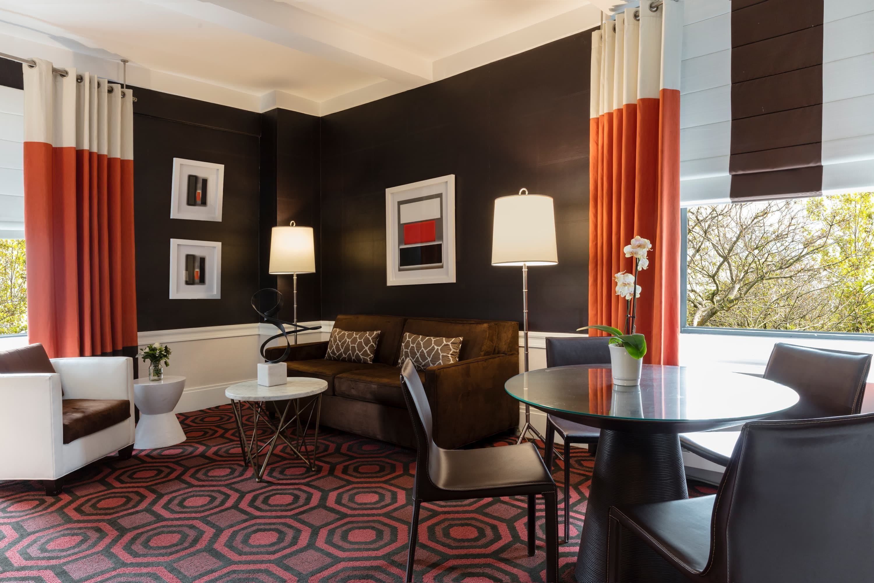 A modern hotel room with a black and white color scheme, a round glass table, a brown sofa, and a white armchair.